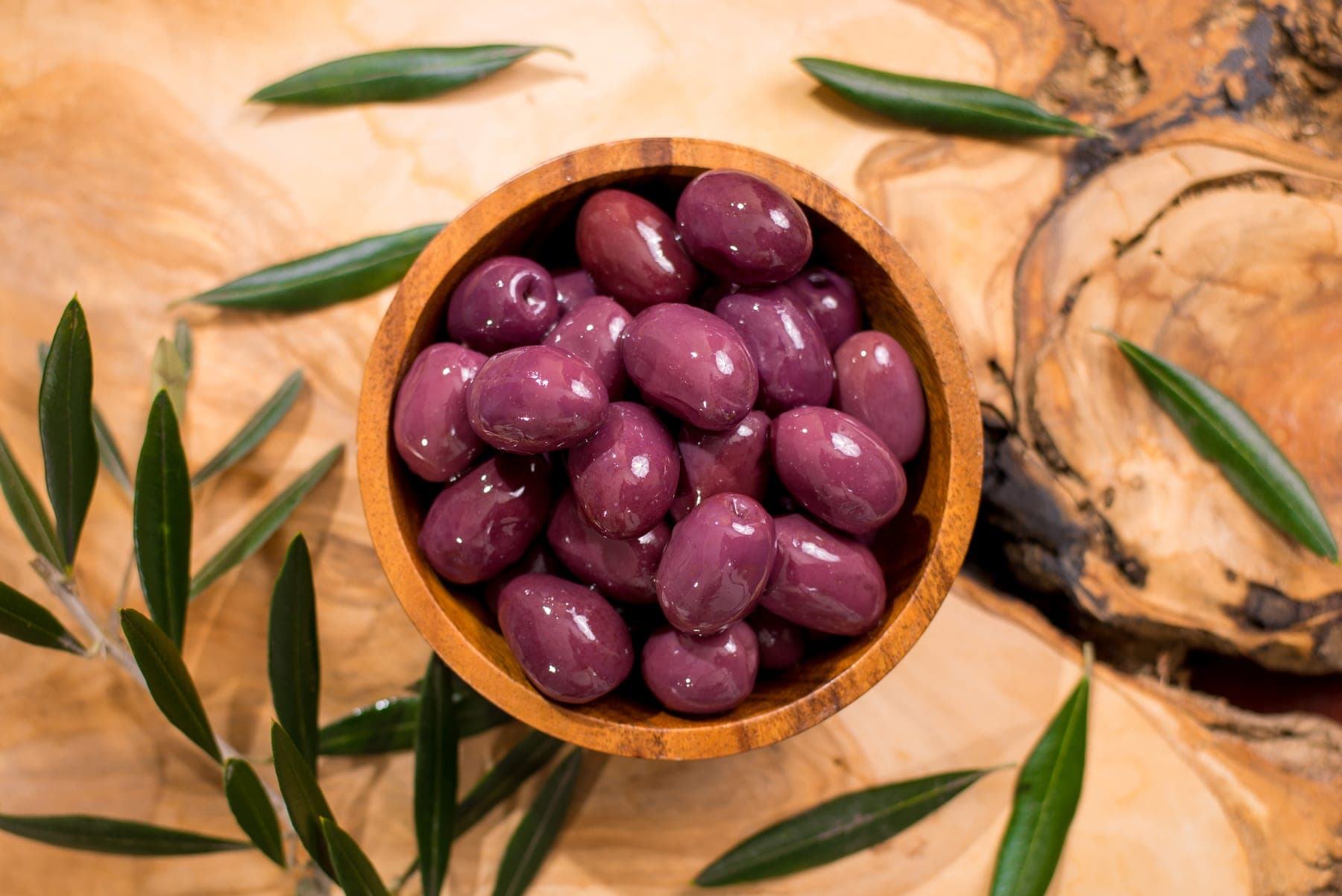 Natural black botija olives in a wooden bowl, seen from above, with olive branches